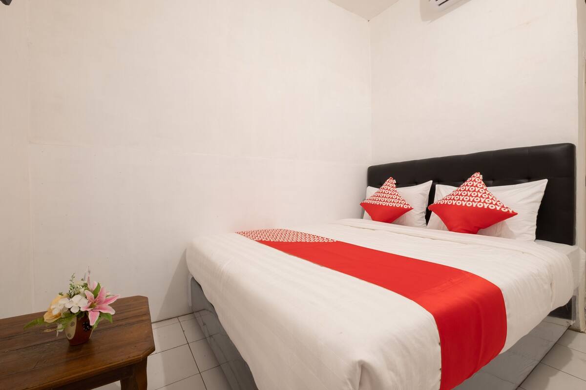 A hotel room with a bed, pillows, a nightstand, and a vase of flowers.