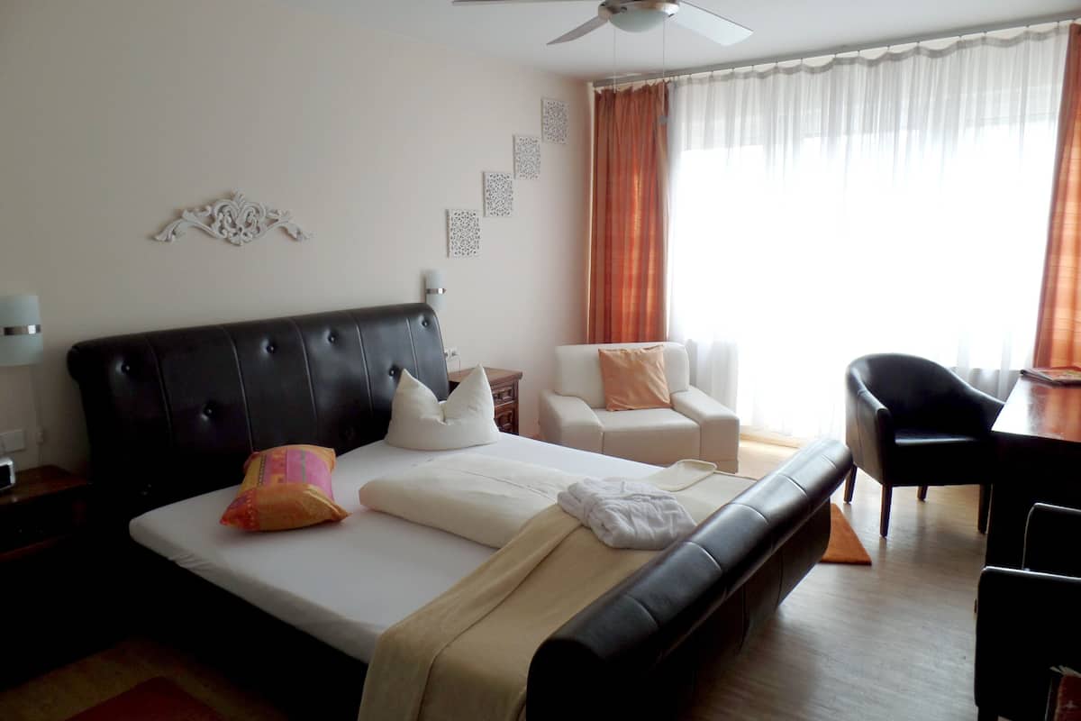 Habitación de hotel con una cama grande, una silla, un escritorio y un ventilador de techo.
