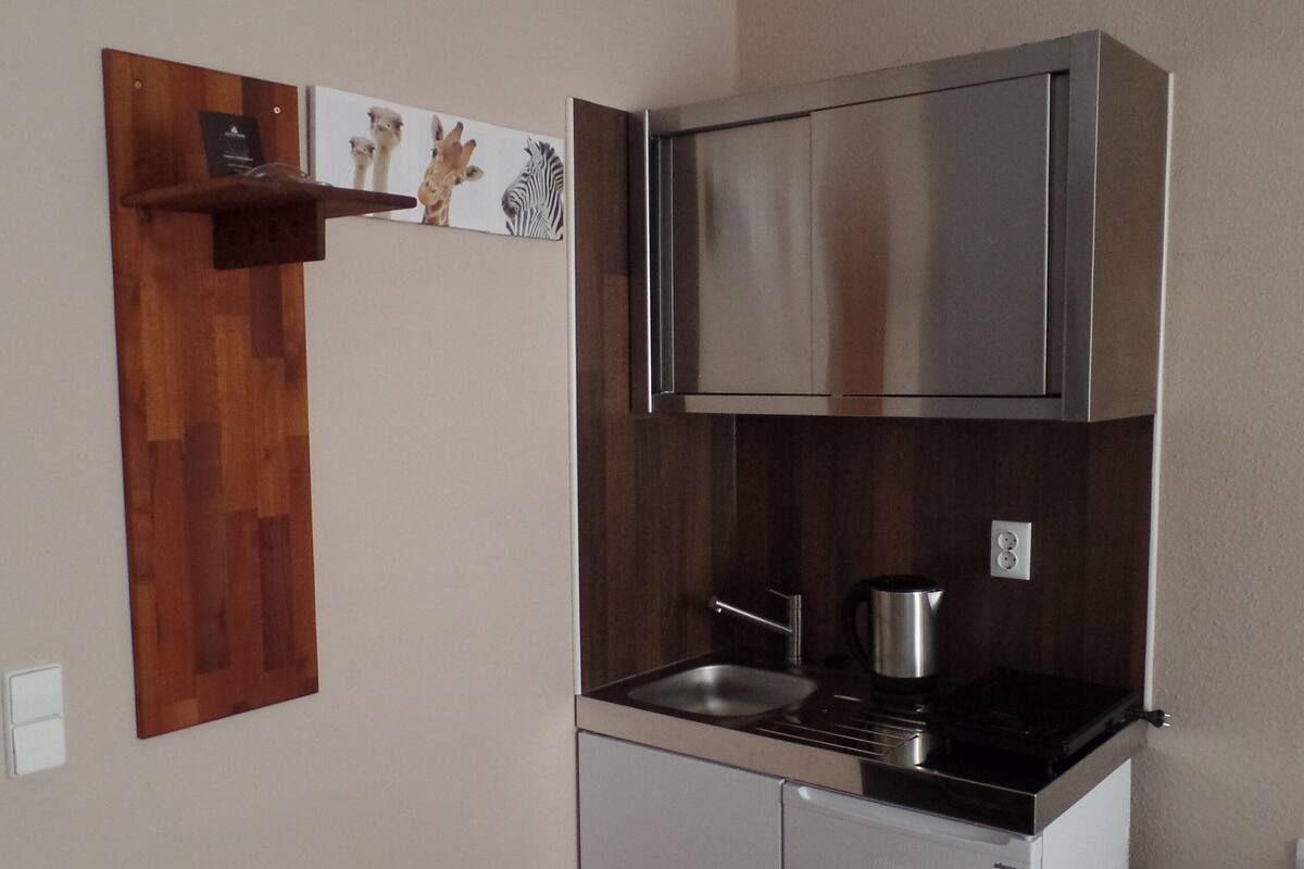 Una cocina compacta con extractor de acero inoxidable, lavamanos integrado y una cafetera pequeña.