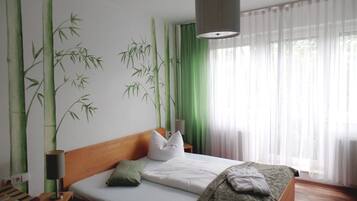 Ein Schlafzimmer mit Bett, Kissen, einer Nachttischlampe, einem Fenster mit durchscheinenden Vorhängen und einer Wandmalerei von Bambus.
