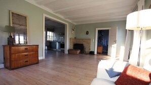 A spacious living room with a wooden floor, a white sofa with a red cushion, a wooden dresser, and a fireplace. - Idyllic holiday home on a listed farm (Natendorf)