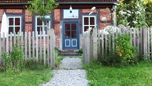 A brick house with a blue door and a wooden picket fence. - Idyllic holiday home on a listed farm (Natendorf)
