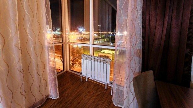 Ein Balkon mit Blick auf eine nächtliche Stadtansicht, mit einem weißen Heizkörper und einem Sessel.