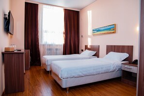 A hotel room with two beds, wooden flooring, a desk, a chair, a TV, and a painting on the wall. - Atlas Hotel (Astana)