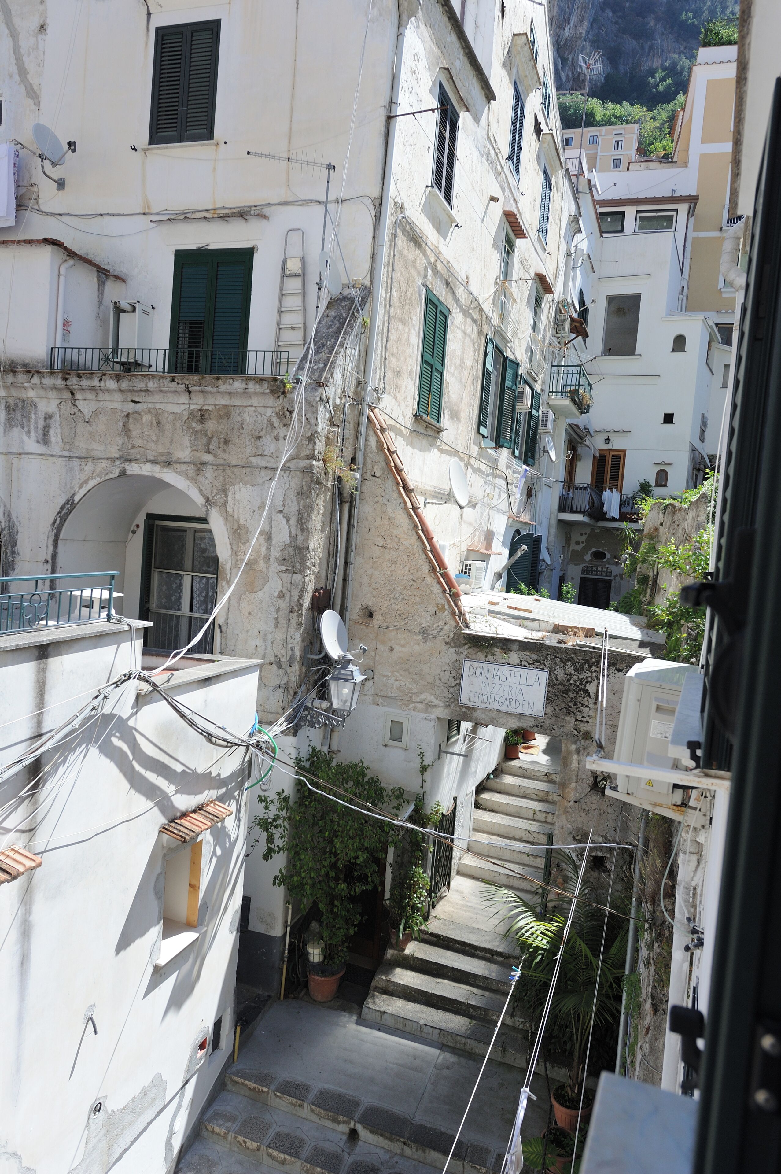 Une rue étroite bordée d’immeubles, avec un escalier et des plantes en pot.