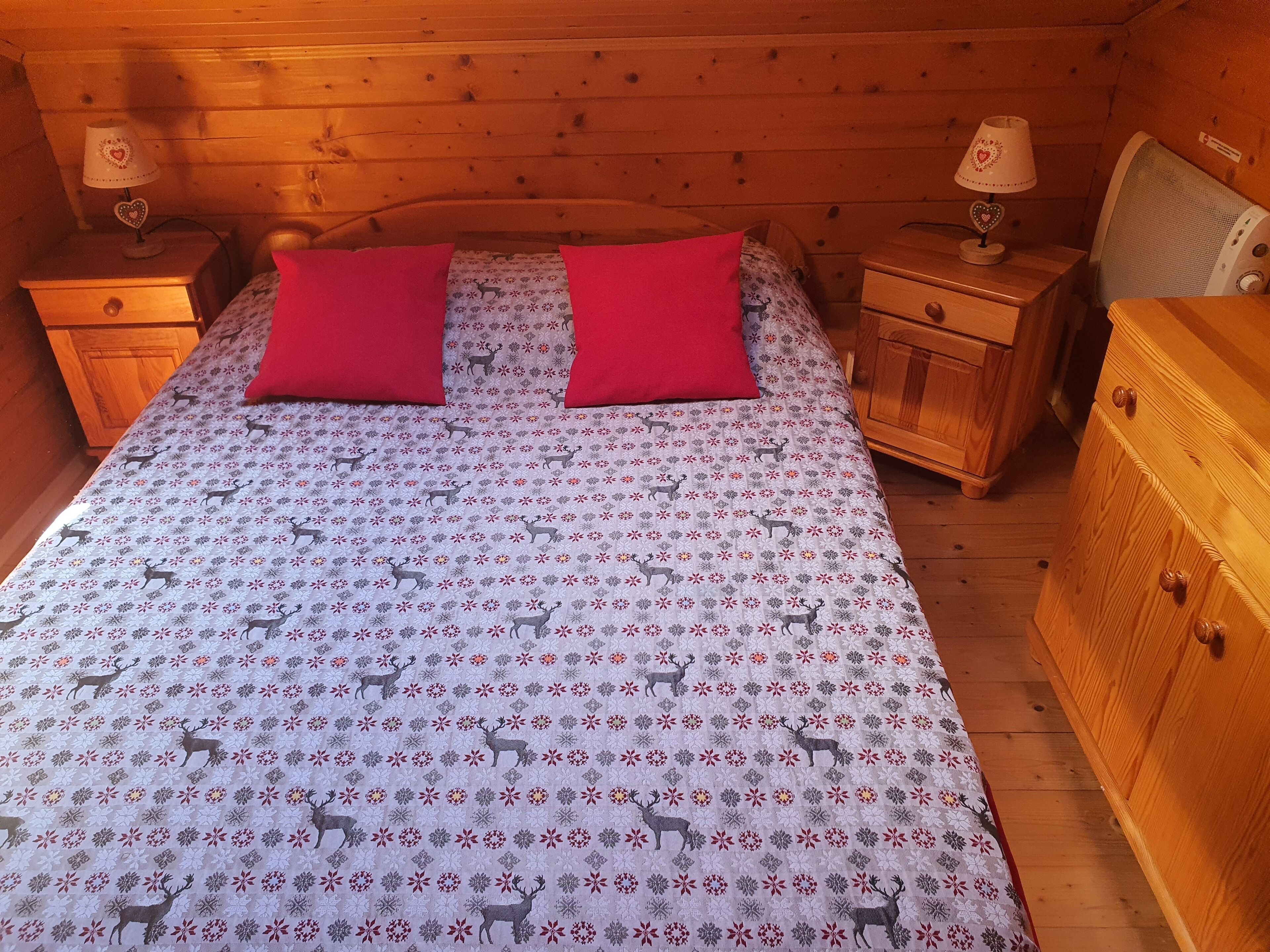Une chambre à coucher dans une cabane en bois, avec un lit agrémenté d’une couvre-lit à motifs, de deux oreillers rouges et de deux tables de chevet avec des lampes.
