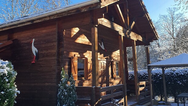 A wooden cabin with a porch, surrounded by snow-covered ground and trees.