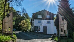Un bâtiment à deux étages, sur lequel on peut voir une enseigne indiquant qu’il s’agit d’un hôtel. Une voiture est garée devant, et le soleil brille de mille feux.