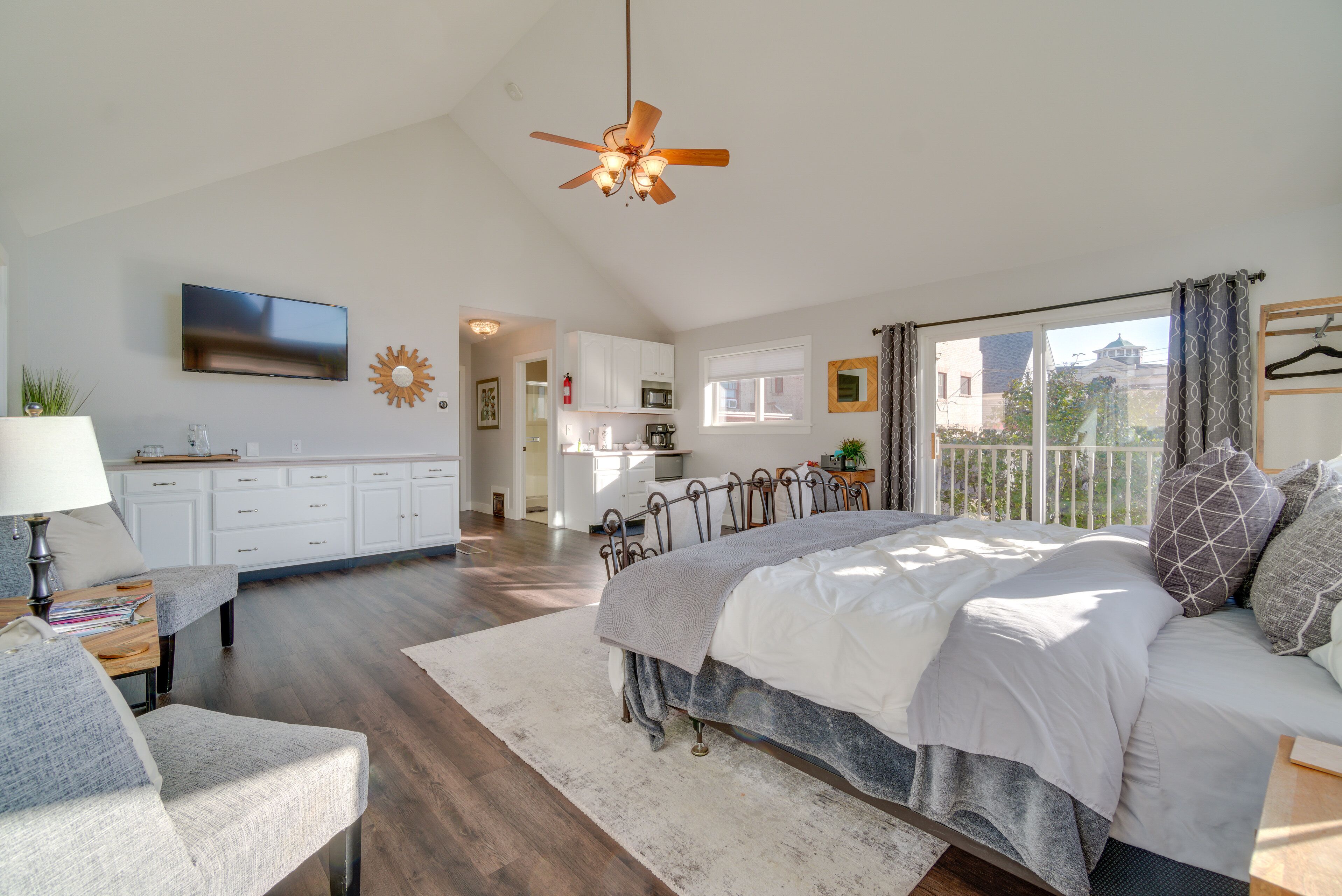 A spacious bedroom with a large bed, a ceiling fan, a TV, and a view of the city through the window.