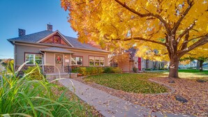 Ein Haus mit einem Steinkamin, einer Veranda und einem gepflegten Rasen mit Herbstlaub.