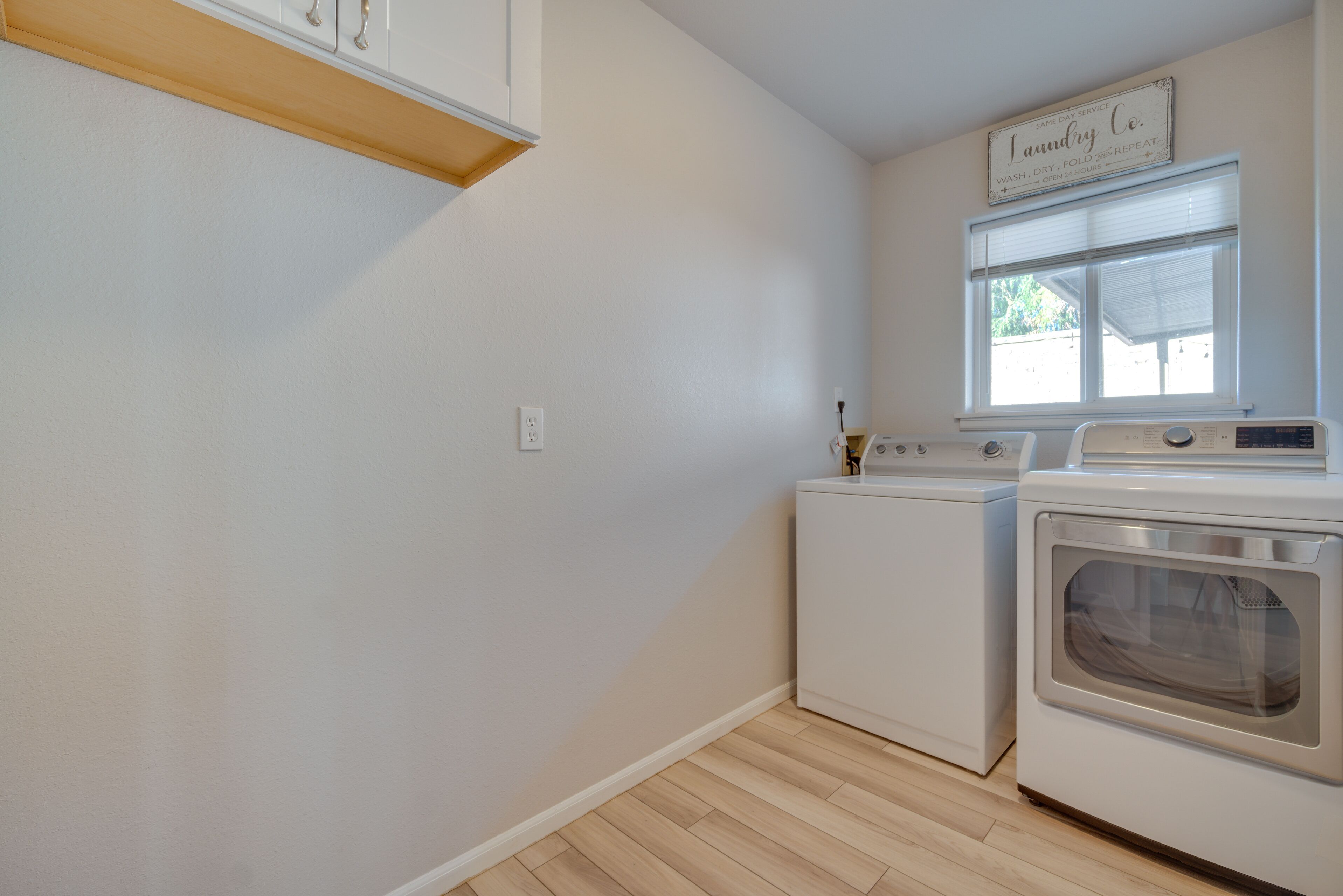A laundry room with a washing machine, dryer, and a sign above the window.