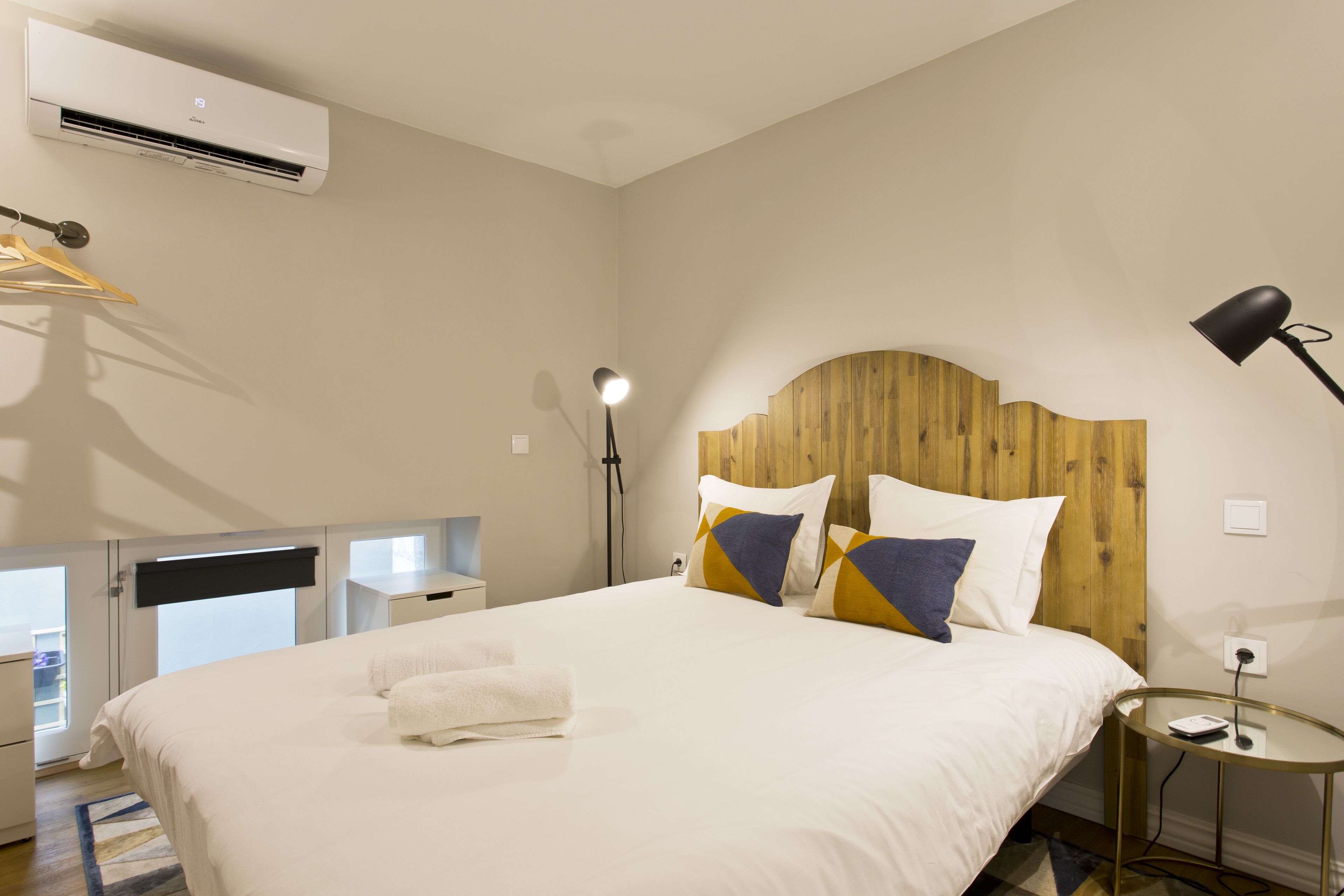 Habitación de hotel con cama, cabecero de madera, mesita de noche, lámpara y equipo de aire acondicionado.