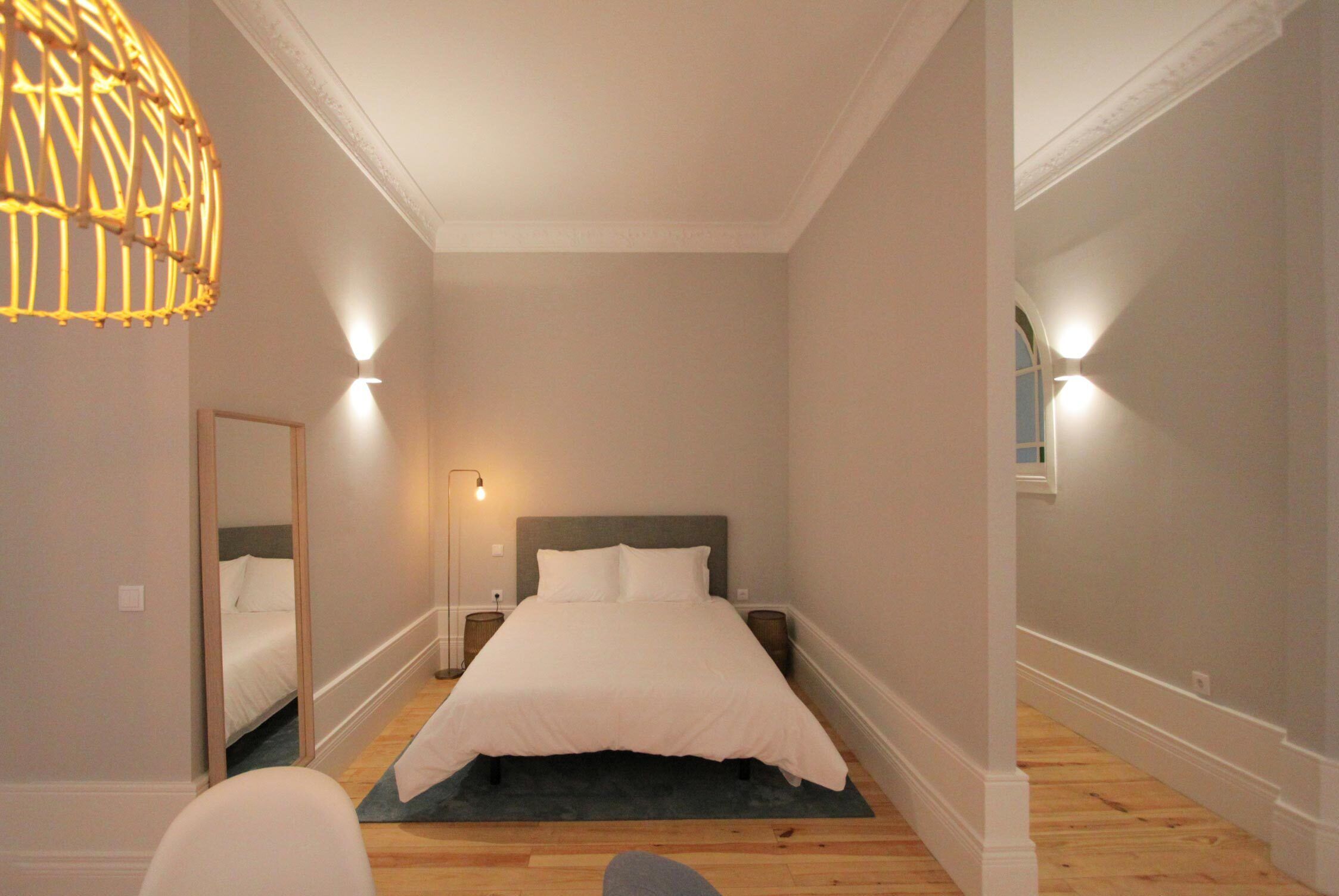 A bedroom with a large bed, bedside lamps, a mirror, and a hanging light fixture.