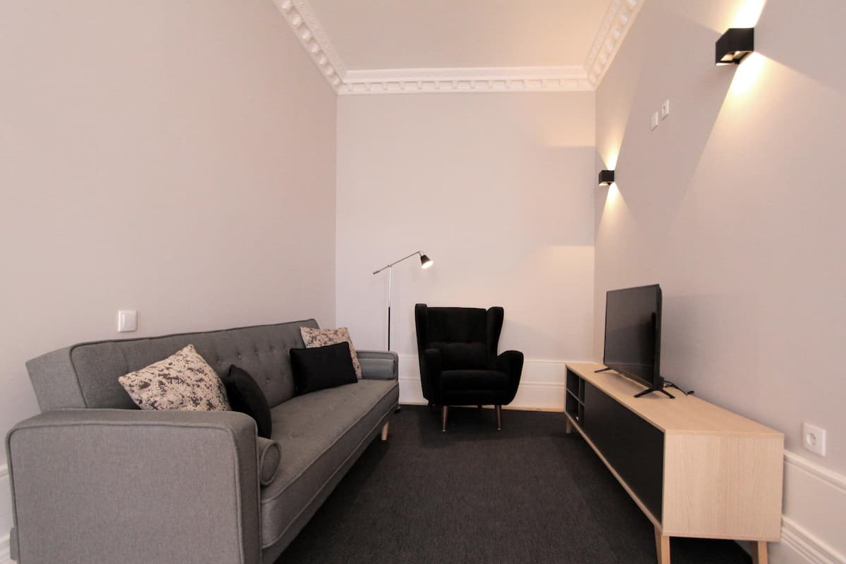 A modern living room with a grey sofa, black armchair, and a TV on a wooden stand.