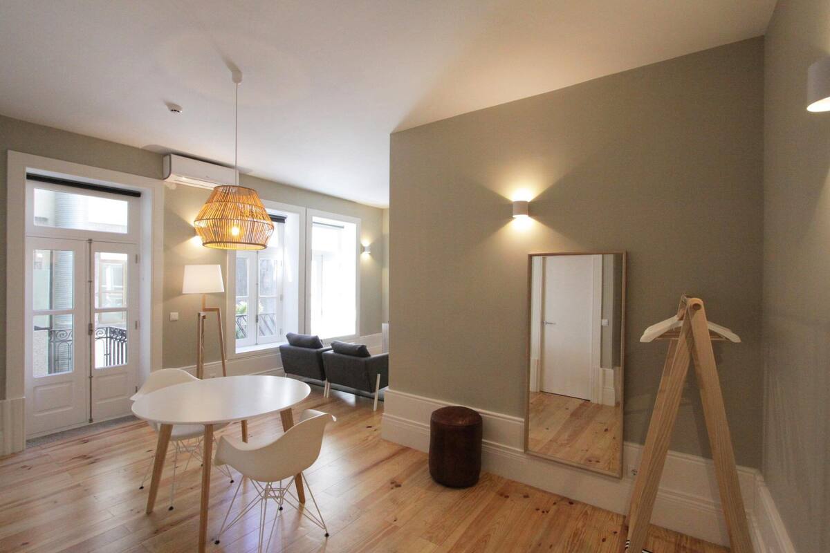 A spacious living room with a white table, chairs, a hanging light fixture, a large mirror, and a wooden easel.