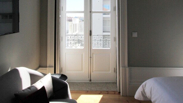 A room with a sofa, a bed, a patterned rug, and a door leading to a balcony. - Duque de Loulé (Porto)
