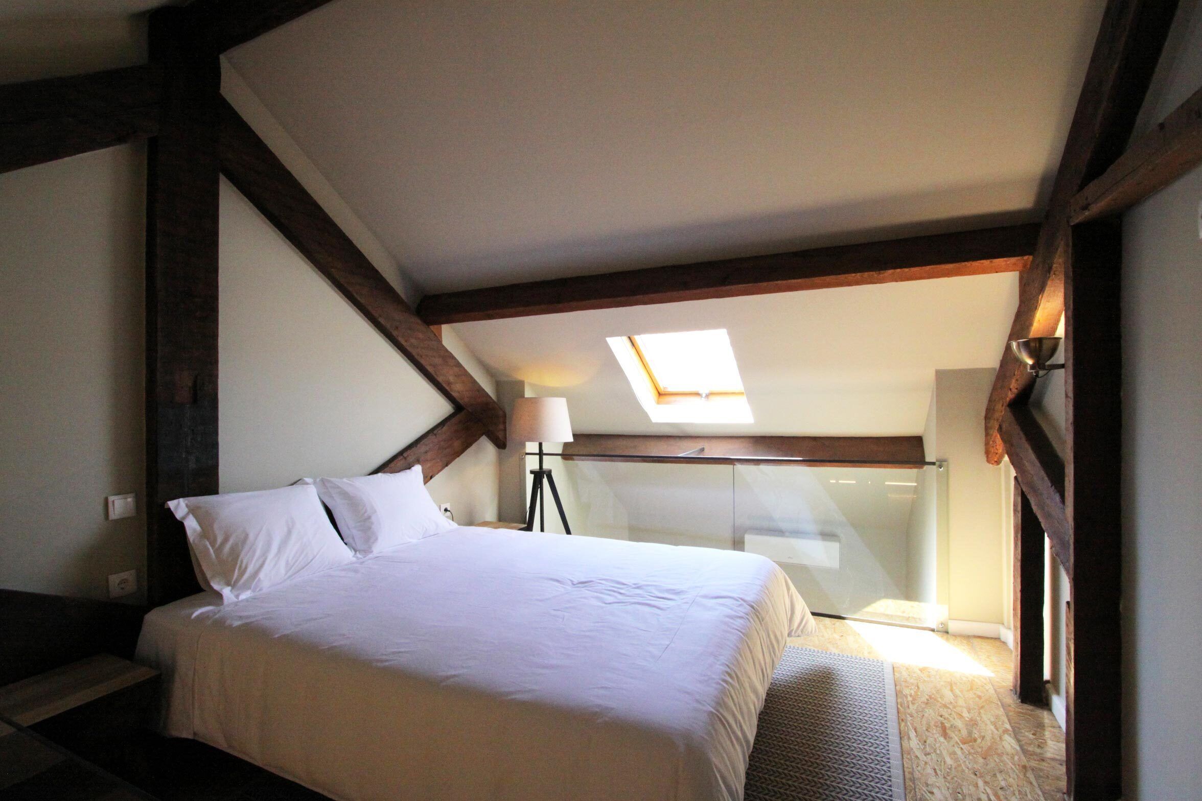 A bedroom with a bed, a skylight, and a nightstand with a lamp.