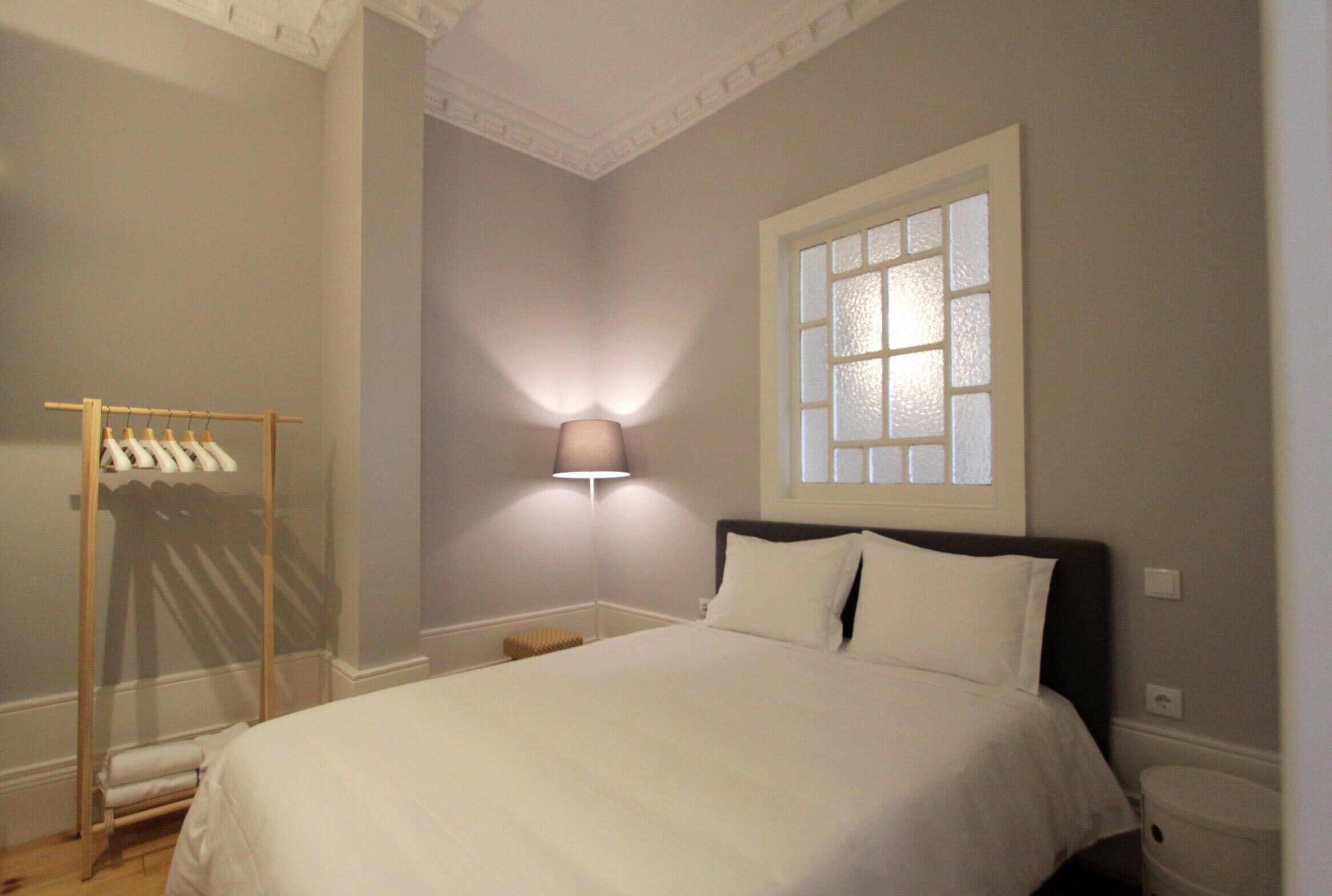 A bedroom with a bed, a wall-mounted lamp, a window, and a clothing rack.