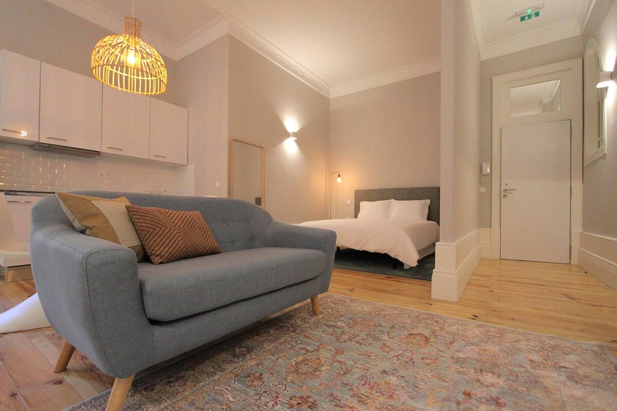 A modern living room with a grey sofa, a patterned rug, and a hanging light fixture.