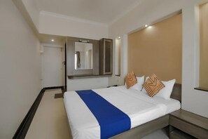 A hotel room with a large bed, a bedside table, a mirror, and a wardrobe. - Royal Regency Lodge (Bengaluru)