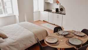 Ein moderner, hell erleuchteter Raum mit einem Bett, einem Esstisch für vier Personen und einer Küchenzeile.