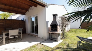 A patio with a wooden table and chairs, a stone-built outdoor oven, and a grassy yard.