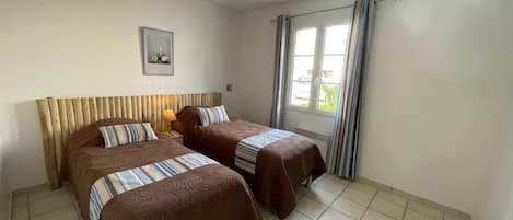 A hotel room with two beds, a wooden headboard, a window with curtains, and a single light fixture.