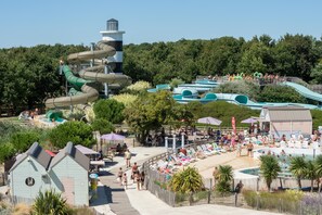 Ein Wasserpark mit zahlreichen Rutschen und Pools, umgeben von Bäumen und einem Strandbereich mit Liegestühlen.