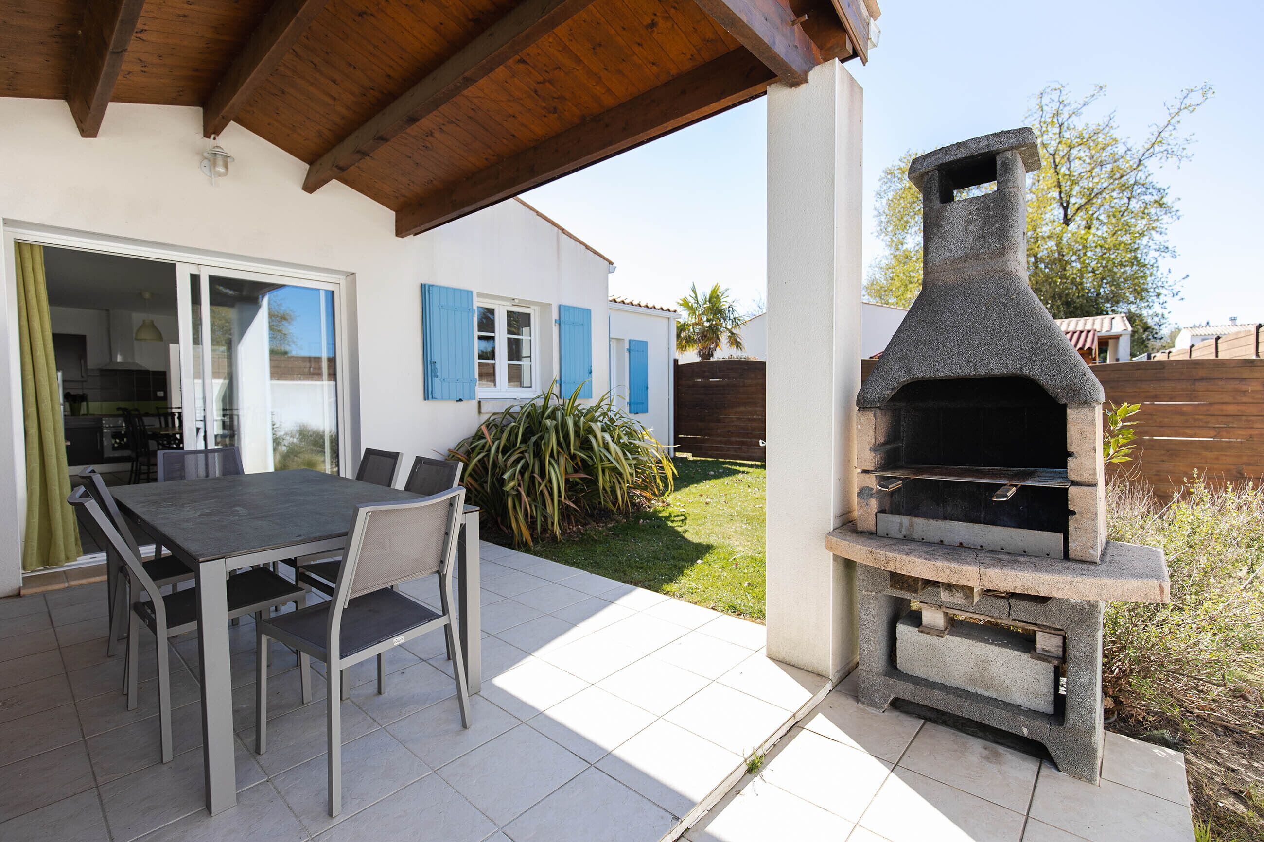 Eine Außenpatio mit einem Steingrill, einem Esstisch mit Stühlen und einem überdachten Bereich mit Holzboden.