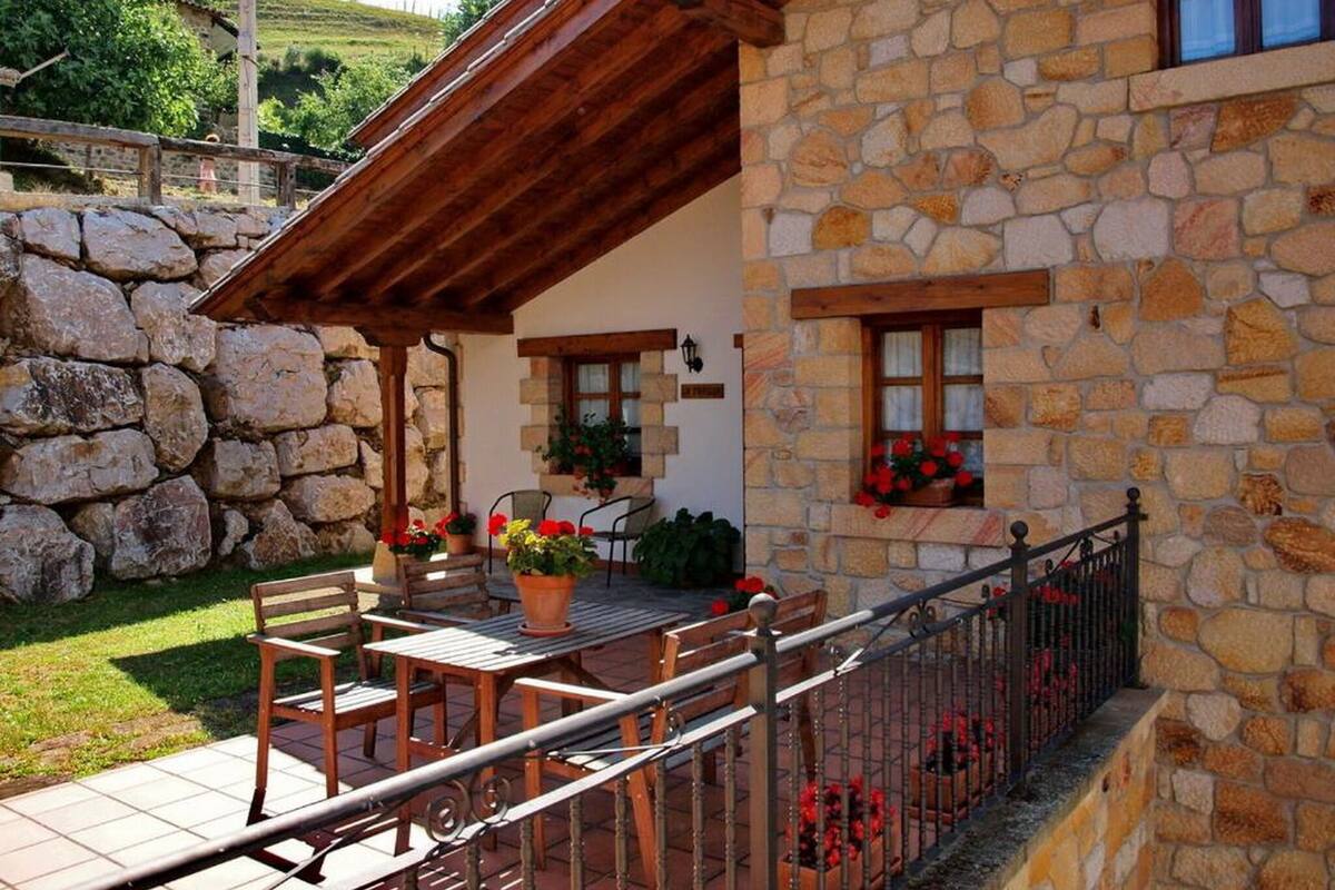 Un edificio de piedra con un balcón de madera, asientos al aire libre y macetas con flores.