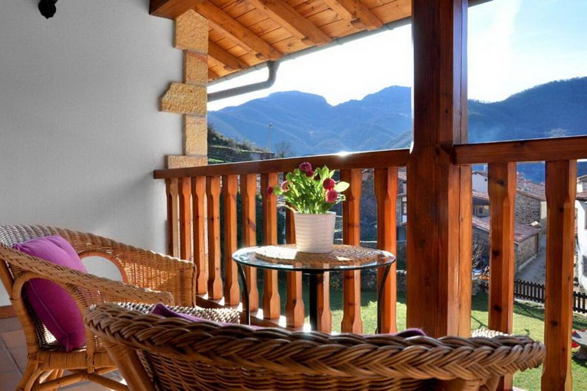 Un balcón con mobiliario de mimbre, una mesa de vidrio con una planta en maceta y vistas a la montaña.