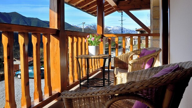 A wooden balcony with wicker furniture, a small table, and a potted plant.