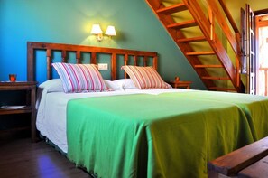A bedroom with a wooden headboard, two bedside tables, a green bedspread, and a sloped ceiling with a wooden staircase. - Viviendas Rurales Los Llares (Pesaguero)