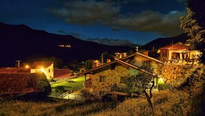 A stone building with a balcony, surrounded by a grassy area and a mountain in the background.