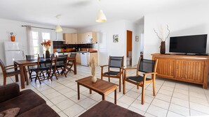 Eine moderne Küche mit Holzschränken, einem Esstisch mit Stühlen, einem Fernseher auf einem Holzboden und einem Sofa im Wohnbereich.