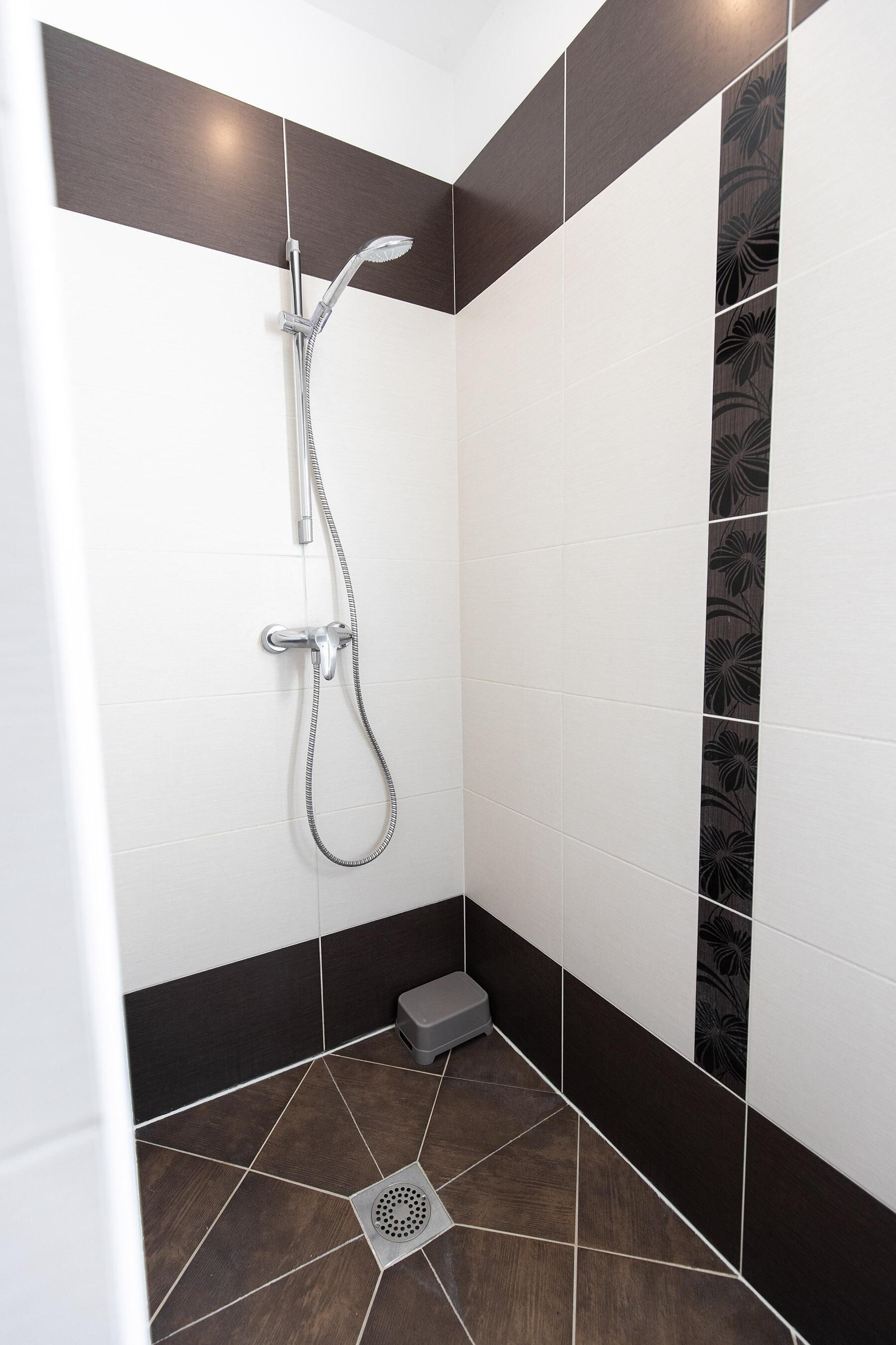 Ducha en esquina con cabezal de ducha de mano y desagüe en el suelo.