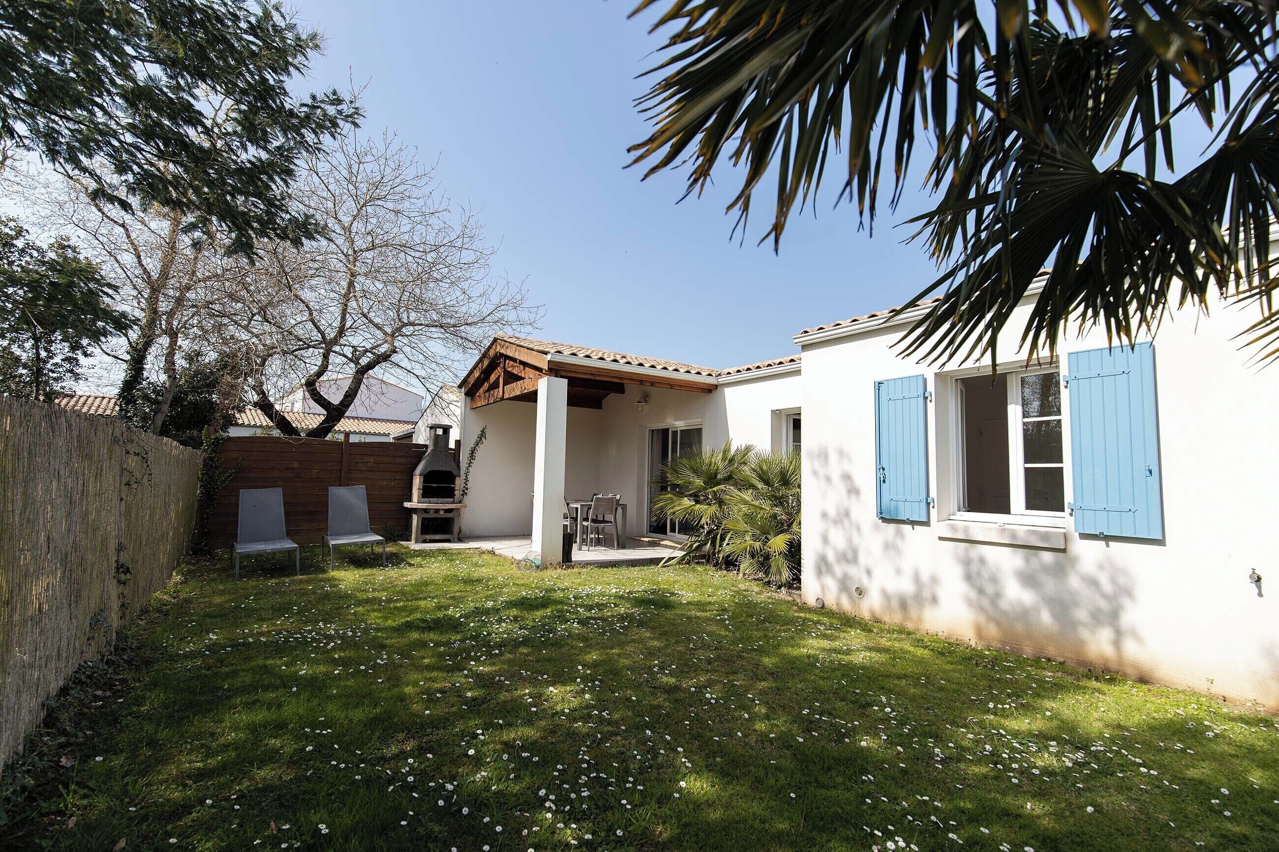 A house with a patio, a wooden fence, and a lawn with white flowers.