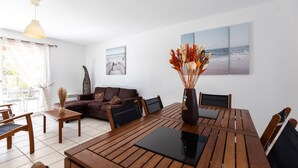 Ein modernes Wohnzimmer mit einem Holzesstisch, einer Couch und einem Couchtisch. Auf dem Tisch steht eine Vase mit Trockenpflanzen.