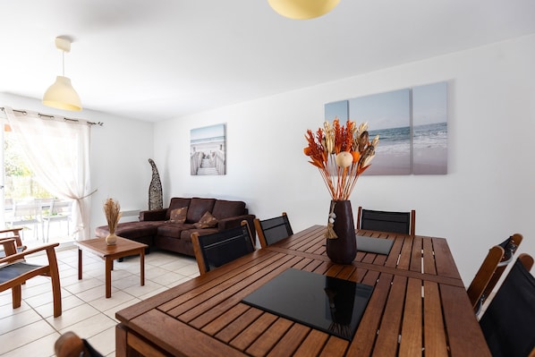 Una sala de estar moderna con una mesa de comedor de madera, un sofá y una mesa de centro. Hay un jarrón con plantas secas sobre la mesa.