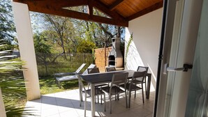 Eine Außenpatio mit Tisch und Stühlen, einem Backofen aus Ziegeln und Blick auf einen Garten.