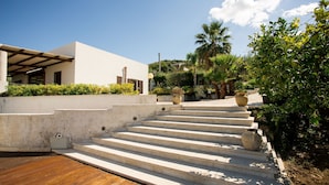 A modern building with a white facade, a wooden deck, and a set of stone steps leading to a covered area. - Independent villa between Trapani and San Vito Lo Capo, with swimming pool and sea view (Valderice)