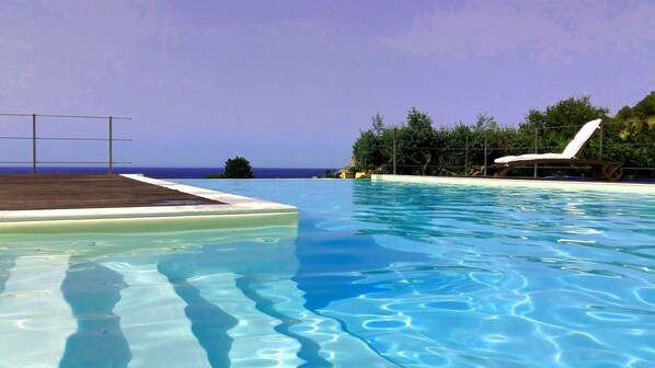 A clear blue pool with a white lounge chair and a wooden deck area. - Independent villa between Trapani and San Vito Lo Capo, with swimming pool and sea view (Valderice)
