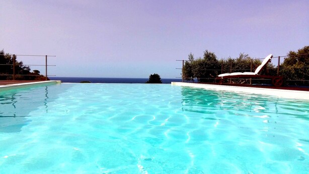 A clear blue pool with a view of the ocean, surrounded by trees and a white lounge chair. - Independent villa between Trapani and San Vito Lo Capo, with swimming pool and sea view (Valderice)