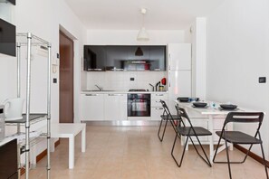 Una cucina moderna con mobili bianchi, forno integrato e zona pranzo con tavolo bianco e sedie nere.