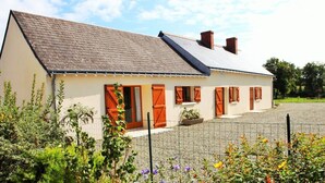 Une maison de plain-pied avec un toit en pente, de nombreuses fenêtres équipées de volets et une cour clôturée.