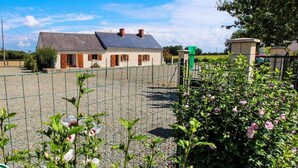 Une propriété rurale dotée d’un espace gravillonné délimité par une clôture, d’une maison avec un toit en pente et de plantes à fleurs au premier plan.