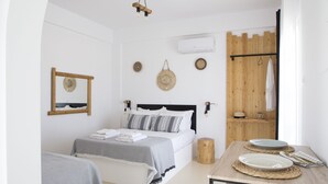A bedroom with a bed, bedside tables, a wooden headboard, a mirror, wall decor, and an air conditioning unit. - Paros King Luxury Apartments (Paros)