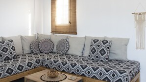 A modern living room with a sectional sofa, a coffee table, and a hanging light fixture. - Paros King Luxury Apartments (Paros)