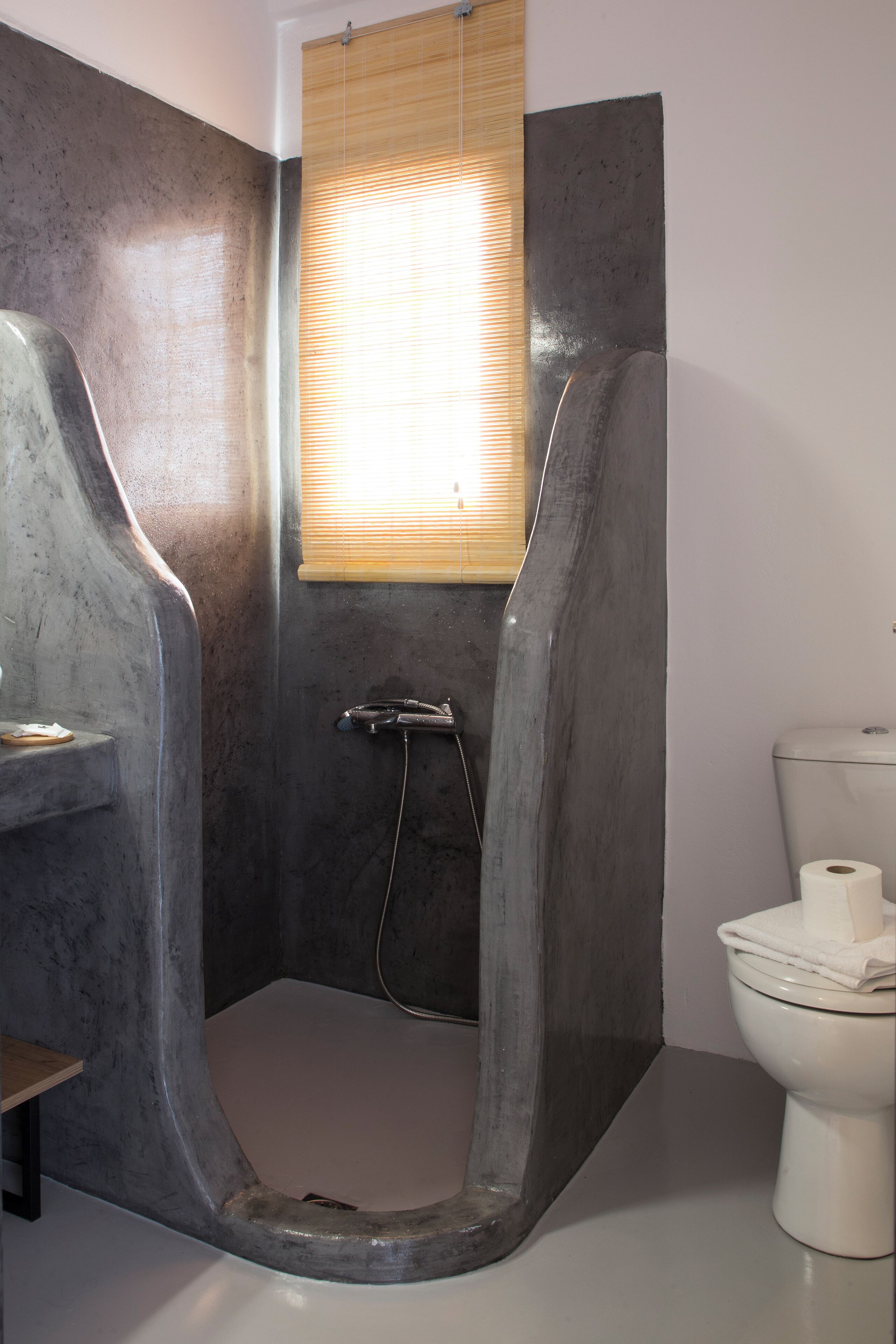 A bathroom with a shower, toilet, and a window with blinds.