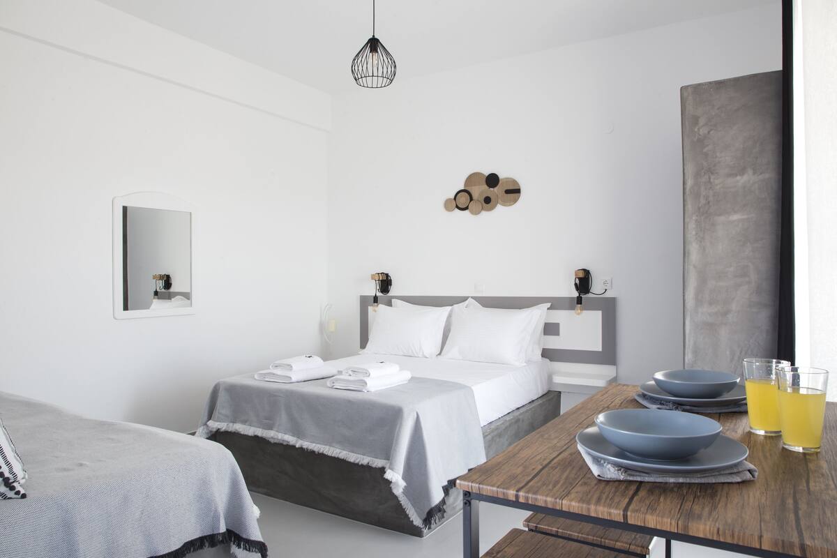 Ein modernes Hotelzimmer mit einem Bett, Nachttischen, einem Holztisch mit Tellern und Gläsern sowie einer Wandleuchte.